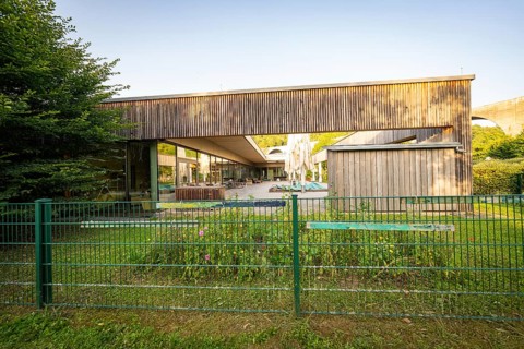 Modern building with wooden wall and garden, surrounded by a green fence in sunshine, Nagold,