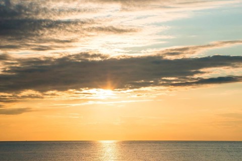 Picturesque sunset over the sea with soft clouds and golden light, sun star, clouds, reflecting