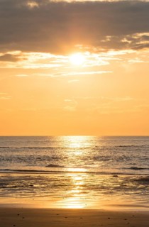 Picturesque sunset over the sea with grey clouds and golden light, sun star, clouds, reflecting