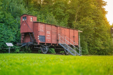 A red goods wagon with steps, green meadow and forest next to it. Nostalgic railway environment,