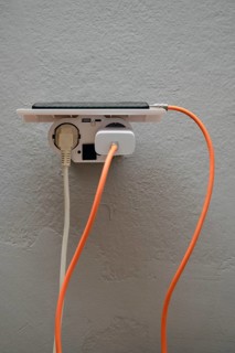 A smartphone is plugged into a wall outlet, showcasing cables in orange and white. This setup