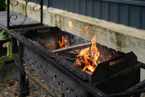 Wood is burning in the grill. The backyard setting features a rustic grill, hinting at a gathering