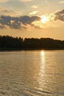 A warm summer afternoon unfolds at the lake, with the sun dipping below the horizon. The water