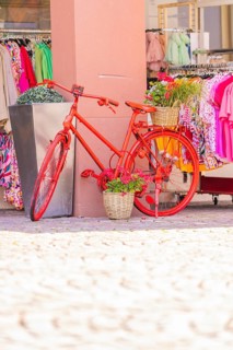 Red bicycle decoratively in front of a clothing shop, surrounded by colourful clothes, small town