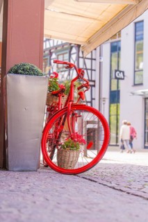 Decorative red bicycle with flower baskets in front of modern buildings in the city centre, small