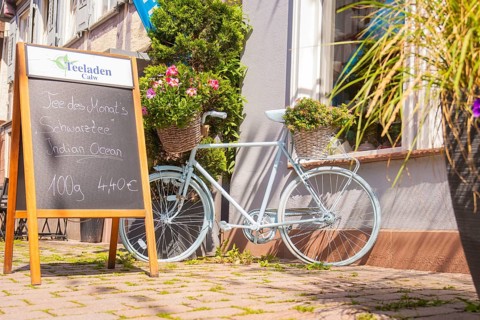A pale bicycle with flowers in baskets next to a chalkboard in front of a café, small town of Perle