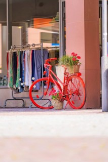 Bright red bicycle with flower arrangement in front of a fashion shop in a sunny street, small town