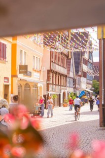 Passers-by and a cyclist in a lively old town street with traditional houses and shops, small town