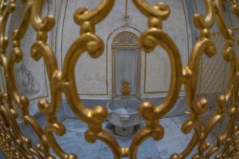 Ornate golden gate protecting a marble fountain inside a historical building in istanbul, turkey,