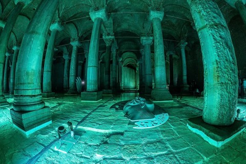 Green lights illuminating ancient columns, medusa's head and hand sculptures in basilica cistern, a
