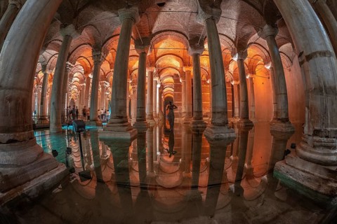Ancient underground basilica cistern reflecting on water surface with tourists and medusa head