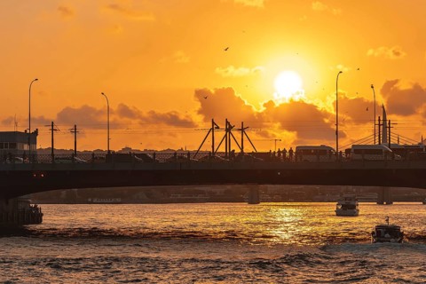 The golden horn waterway in istanbul, turkey, glows under a vibrant sunset, with a bridge full of