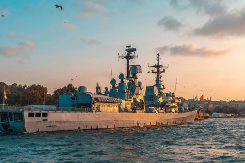 Modern warship gliding through the tranquil sea near istanbul, turkey, under a stunning golden hour