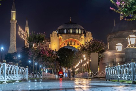 Tourists strolling in front of the hagia sophia mosque, beautifully illuminated at night, creating