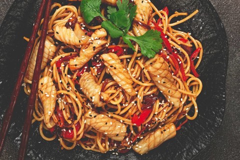Udon noodles, with squid and vegetables, on a black plate, homemade, no people