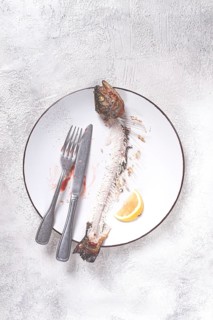 The remains of fish on a plate with a fork and knife, the skeleton of a rainbow trout, after lunch,