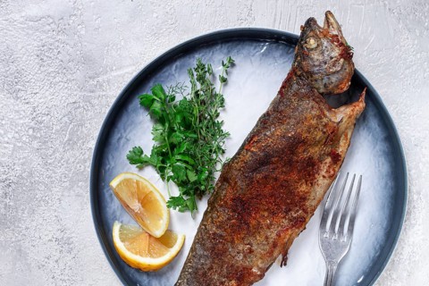 Fried rainbow trout, with herbs and citrus fruits, on a plate, top view