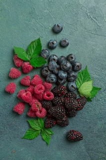 A mix of ripe berries, with leaves scattered on the table, raspberries, blackberries, blueberries,