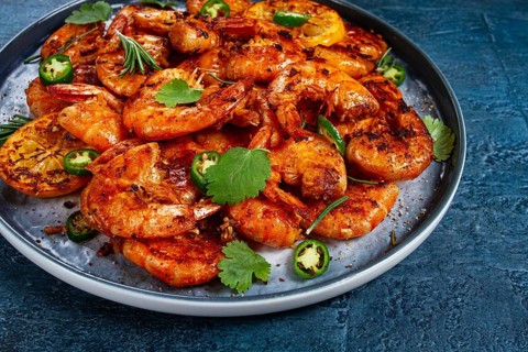 Grilled shrimp, unpeeled, headless, with spices, on a dark blue table, homemade, no people
