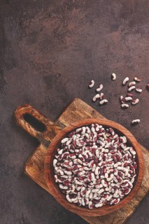 Variegated beans, red with white spots, raw in a wooden bowl, top view, no people