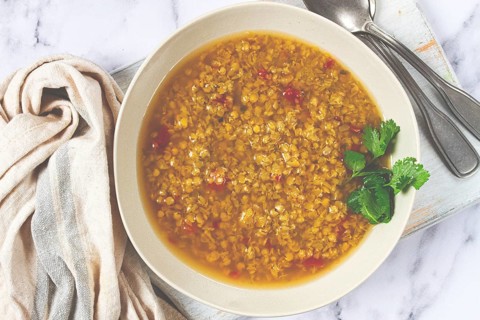 A hearty bowl of lentil soup, rich in flavor and garnished with fresh herbs, is displayed on a