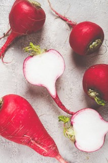 Bright red radishes are arranged on a counter, with one radish cut in half to reveal the crisp
