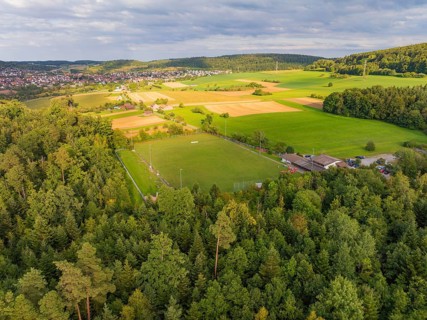 Aerial view of a rural area with a sports field surrounded by forests and fields, close to