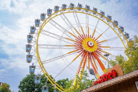 Colourful Ferris wheel with blue cabins, framed by fairground stands, Olympic Park, Munich, Germany
