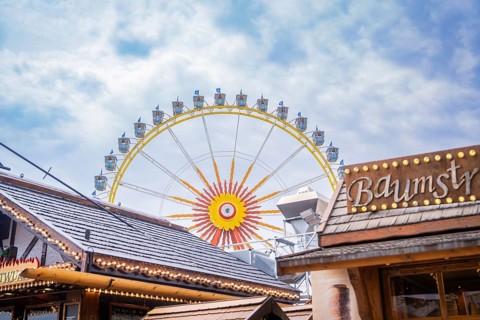 Large Ferris wheel behind wooden buildings, in a bright and cloudy sky, Olympiapark, Munich,