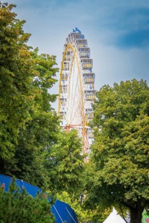 Ferris wheel hidden behind dense green trees under a blue sky, Olympiapark, Munich, Germany