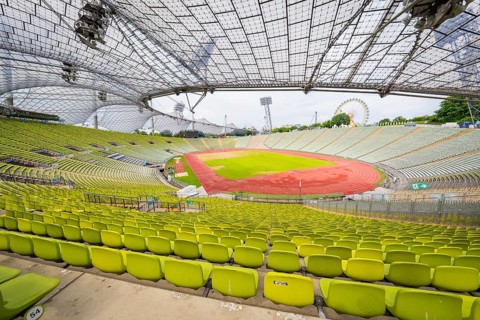 Overview of the stadium with green seats and red running track, framed by an impressive roof