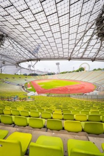 Panoramic view of stadium with yellow-green seats and red running track under a filigree roof,