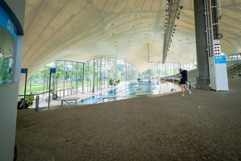 View into an indoor swimming pool with large windows that bring a lot of light onto the pool,