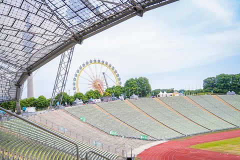 Open stadium with a view of a Ferris wheel in the background and green rows of seats, Olympic Park,