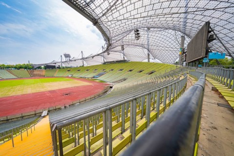 Empty modern stadium with green seats and striking glass roof under a blue sky, Olympiapark,