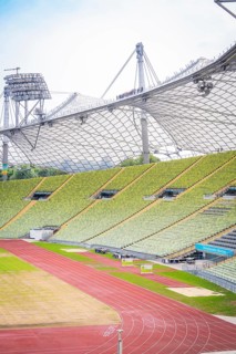 Partial view of a modern stadium with green rows of seats and red running track, Olympic Park,