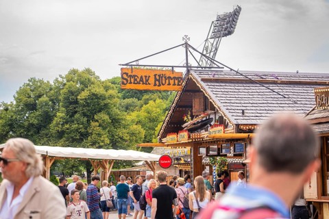 A traditional building with a crowd in front of it, surrounded by nature and advertising,