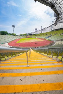 View down the yellow steps to an empty stadium with wide stands and running track, Olympiapark,