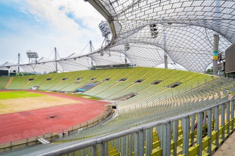 Large stadium with empty green stands and striking roof structure in the sunlight, Olympiapark,