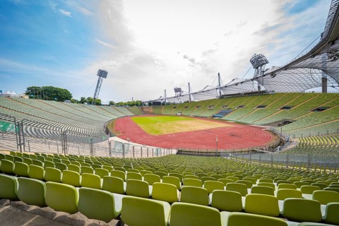 Empty stadium with green seats and a red running track under a bright sky, Olympiapark, Munich,