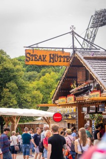 Traditionally designed hut with lettering, surrounded by people and green background, Olympic Park,