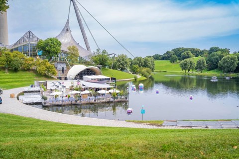 Idyllic landscape with lake, modern pavilion and grassy hills, Olympic Park, Munich, Germany