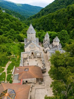 Aerial view of an old monastery complex surrounded by lush green forests, showing historical
