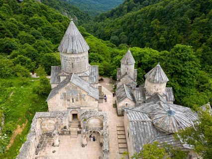 Historic stone monastery building, embedded in a wooded hilly landscape, aerial view, Haghartsin