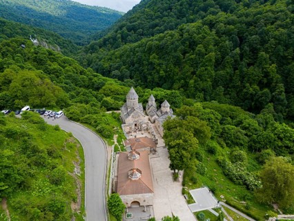 Monastery on a winding road, surrounded by dense natural vegetation and hills, aerial view,