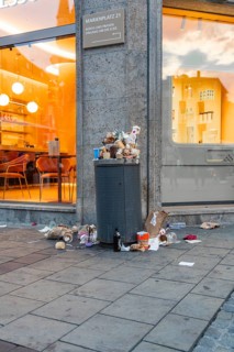 An overfilled rubbish bin with waste on the pavement in front of a shop, Marienplatz, Munich,