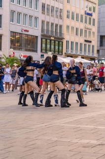 Dance group performs outdoors against an urban backdrop, surrounded by spectators, Munich, Germany