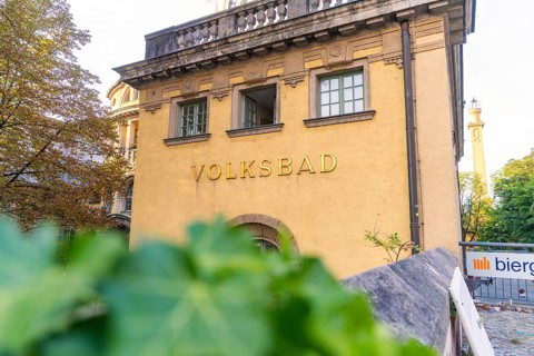 Historic public swimming pool with yellow façade, traditional architecture and surrounded by trees,