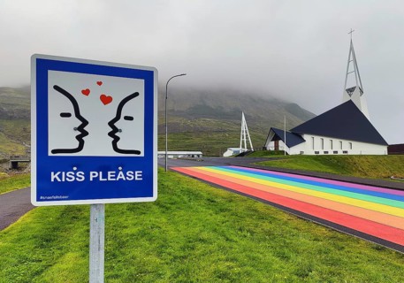 Sign with the invitation to kiss with a street painted in the colours of the rainbow and the