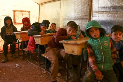 Syrian refugee children sitting inside a tent classroom, receiving basic education despite
